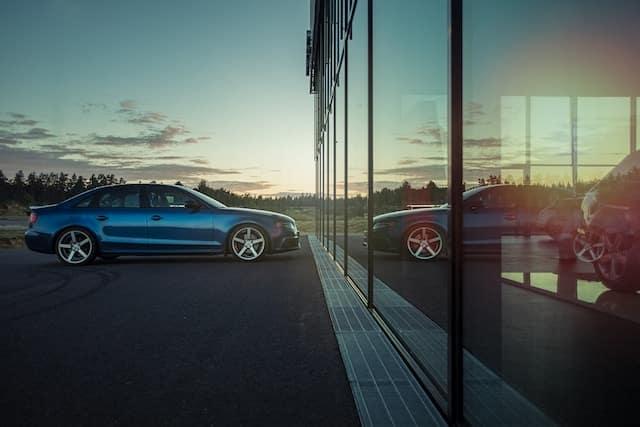 Buying a car in Iceland: sleek blue car parked by a glass building at sunset.