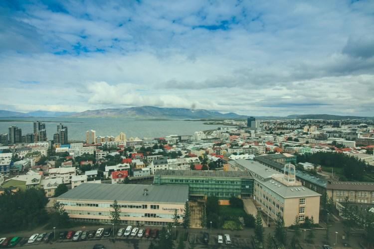 Panoramic view of Reykjavik, Iceland, showcasing the cityscape with colorful buildings, the ocean in the distance, and mountains under a cloudy sky, highlighting the unique geography of the capital.