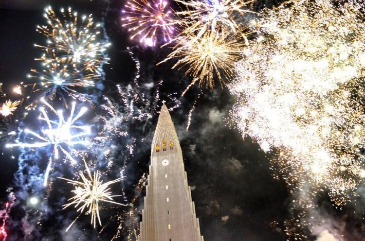 Fireworks exploding over Hallgrímskirkja church in Reykjavik, Iceland, celebrating the New Year with vibrant colors lighting up the night sky.
